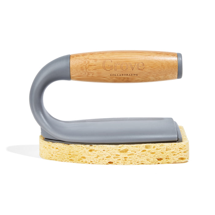 The Tub Handler by Grove Co. is a dish brush with a wooden handle and gray body, featuring a sponge at the base and replaceable brush heads. Its Grove Collaborative-engraved handle includes recycled plastic for sustainability, standing upright against a white background.