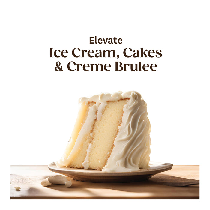 A slice of cake made with Heilala Vanilla Paste and white frosting sits on a wooden plate. The background is plain white, featuring the text Elevate Ice Cream, Cakes & Creme Brulee above the cake.