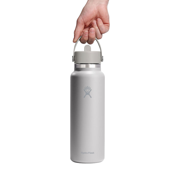 A hand holds a 40 oz light gray Hydro Flask Wide Mouth Bottle with Flex Straw Cap and handle, featuring the logo and Hydro Flask inscribed near the bottom.