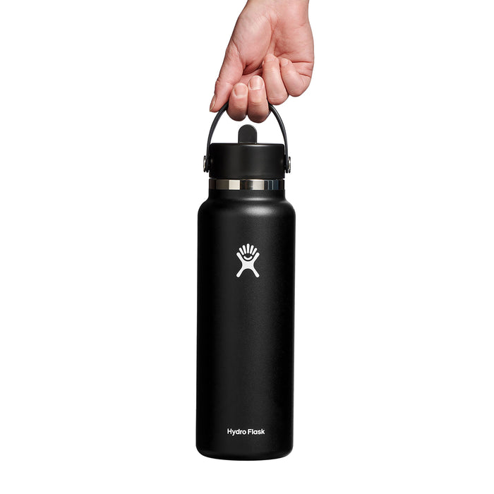 A hand showcases a sleek black Hydro Flask with its logo and text. The Wide Mouth Bottle with Flex Straw Cap, 40 oz is perfect for on-the-go use against a clean white backdrop.